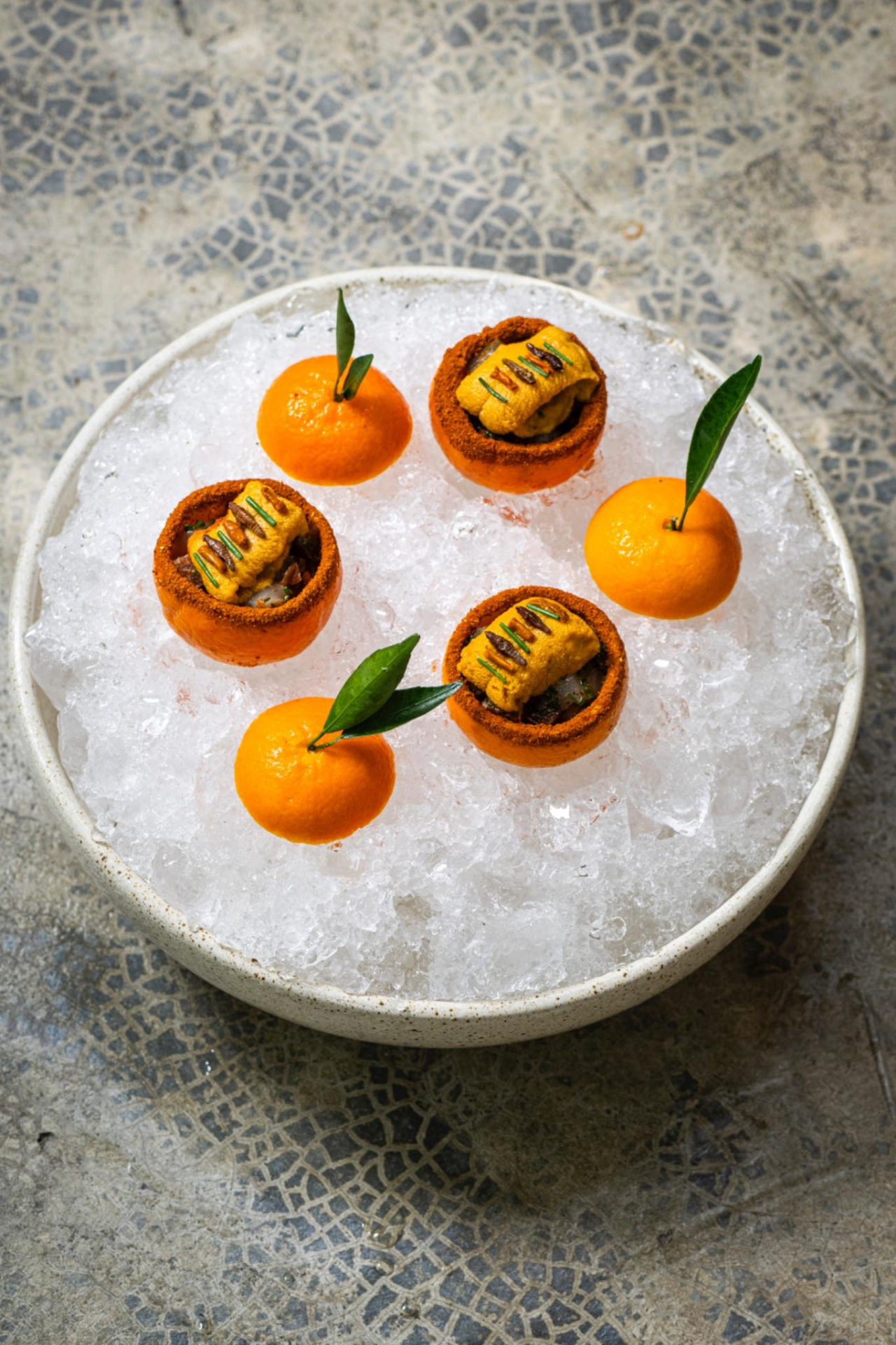 Mandarinas con erizo de mar y caracol servidas sobre hielo picado en plato blanco, ARCA Tulum